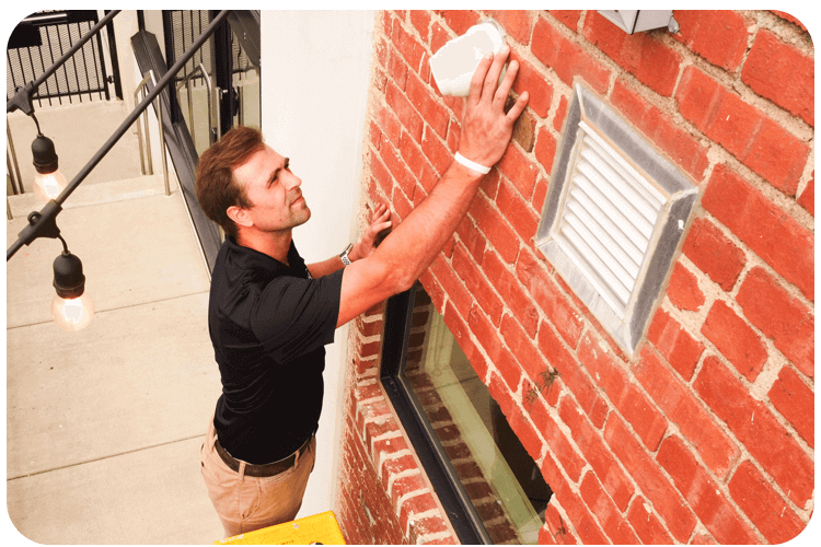 Businessman checking a security camera mounted on a brick wall outside a building in Phoenix, AZ.